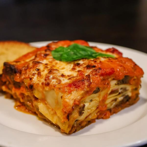 A slice of lasagna with melted cheese and red sauce, garnished with a basil leaf.