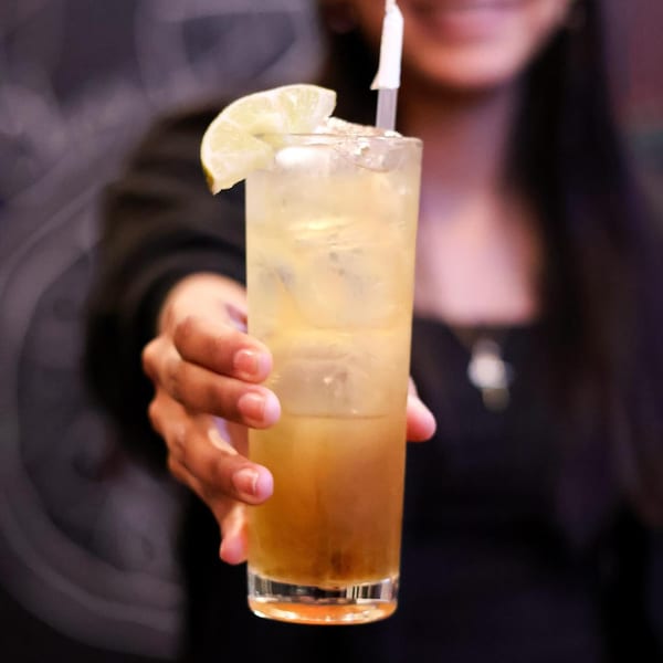 A person's hand holding out a tall glass of iced tea with a lemon slice and straw.