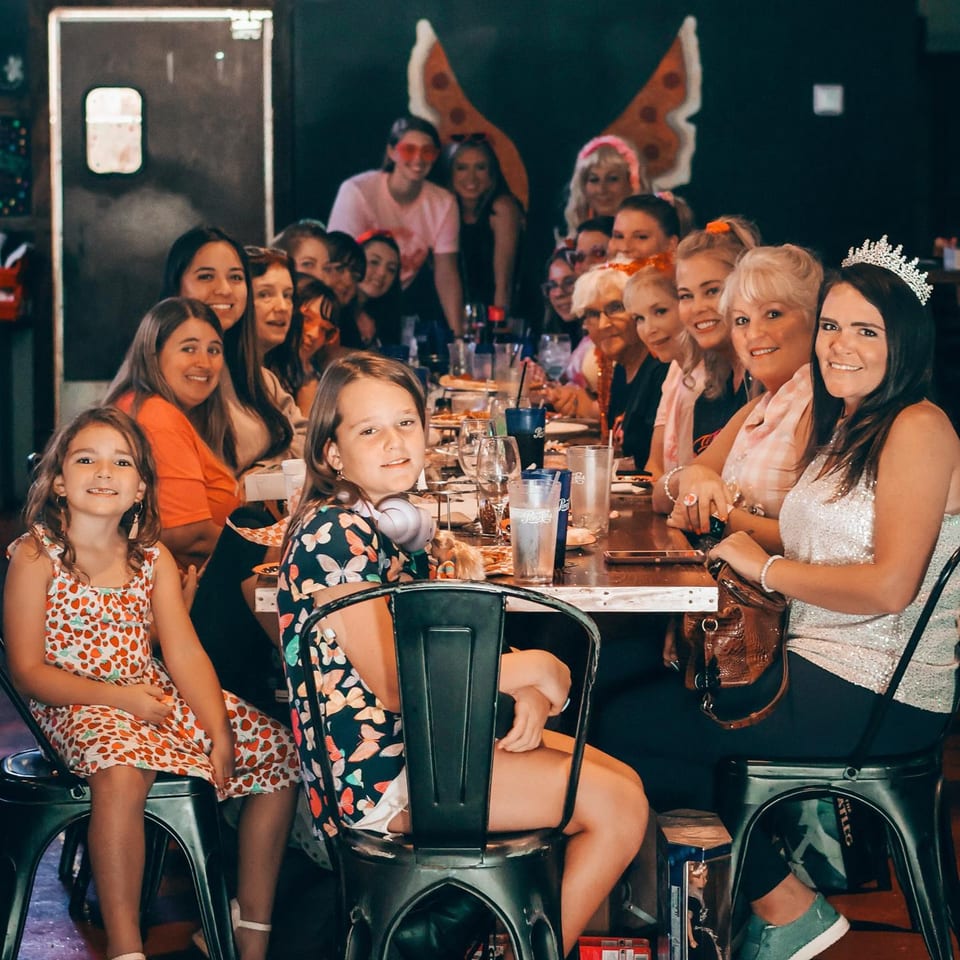 A large group of women and girls smiling at a long table in Up North Pizzeria.