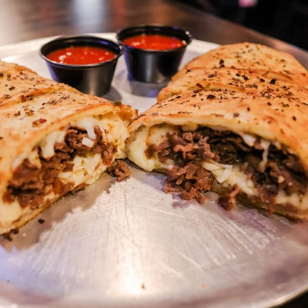 A sliced Up North Pizzeria calzone, filled with meat and cheese, served with two cups of marinara sauce.