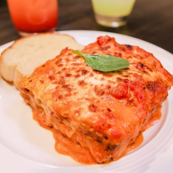 A serving of lasagna with melted cheese and tomato sauce, garnished with basil, next to a slice of bread.