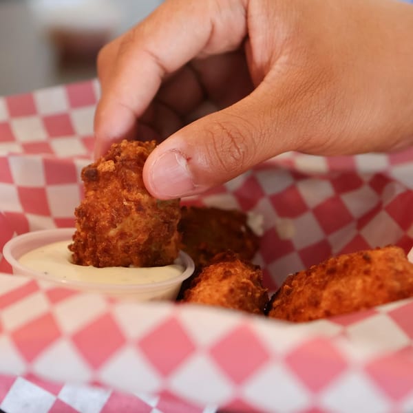Hand dipping a golden-brown fried cheese curd into a small cup of ranch dressing.