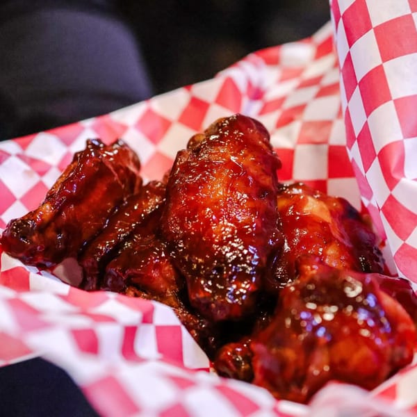 Up North Pizzeria's BBQ chicken wings, glistening with sauce, served in a red and white checkered paper basket.