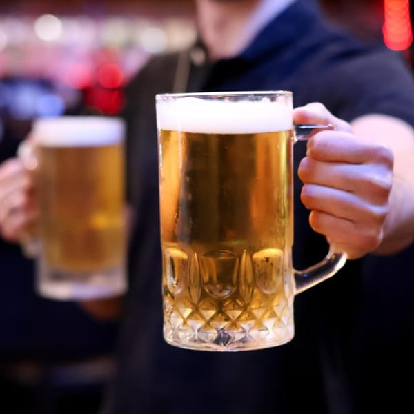 A person holds two frosty mugs of Up North Pizzeria's golden beer with foamy heads.